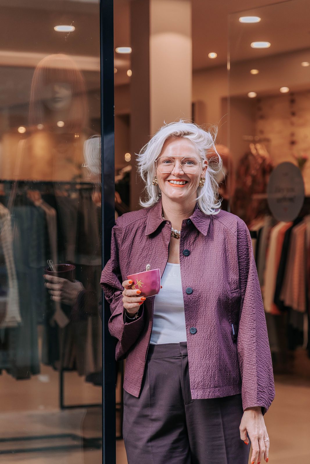 Ellie Thijssen lachend in de deur van KUIF aan de Klaasstraat, met een kop koffie